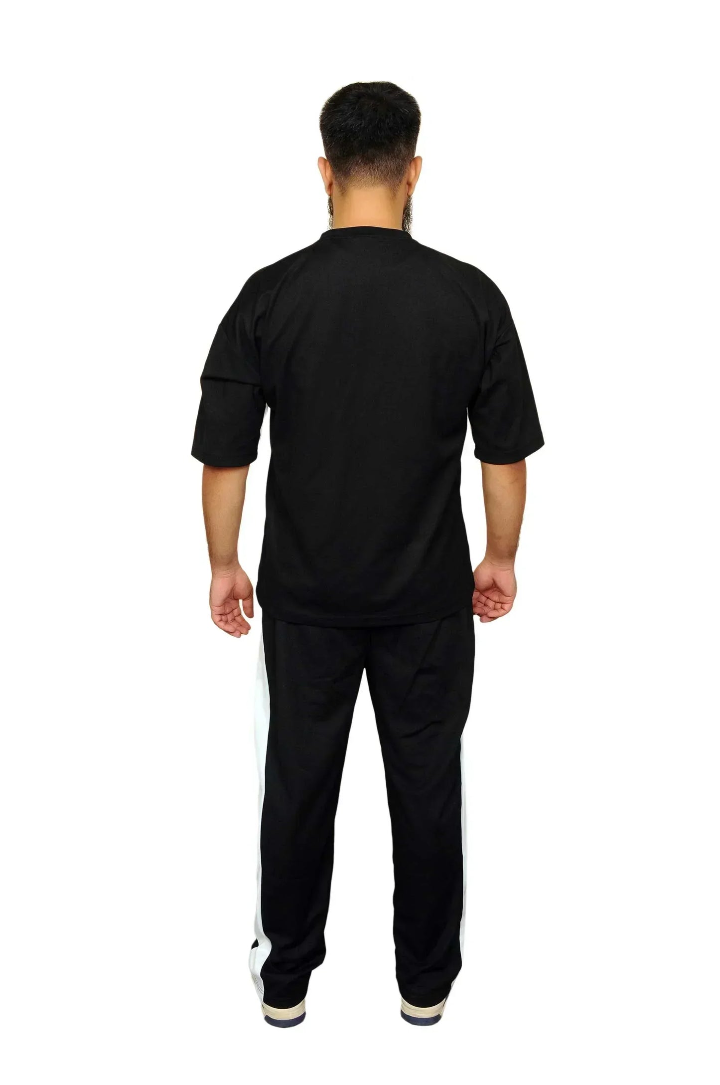 Man wearing black tracksuit with white side stripes, standing facing away on white background