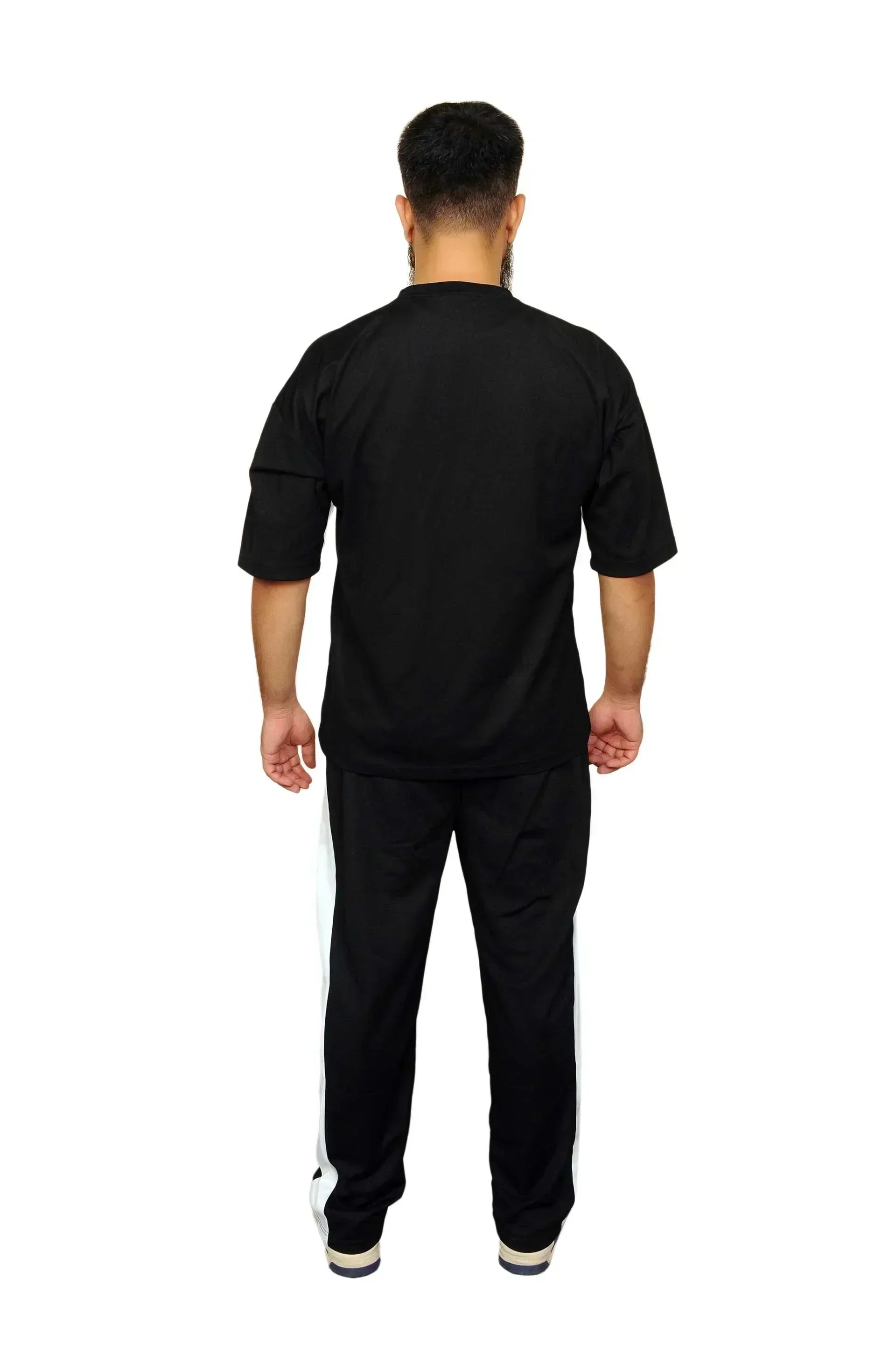 Man wearing black tracksuit with white side stripes, standing facing away on white background