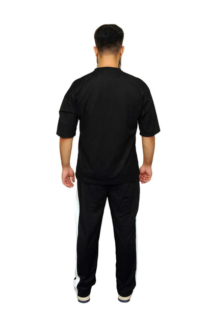 Man wearing black tracksuit with white side stripes, standing facing away on white background