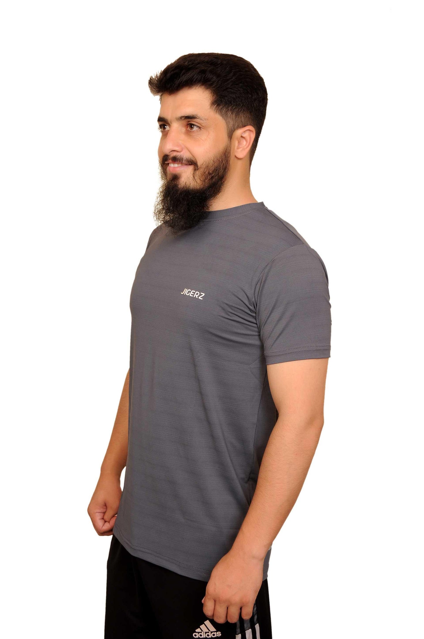 Man wearing grey JIGERZ t-shirt and black Adidas pants standing against white background