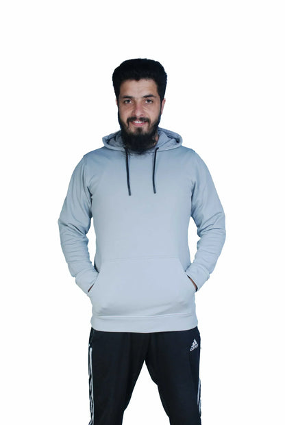 Smiling man wearing light grey hoodie and black Adidas track pants with hands in pockets