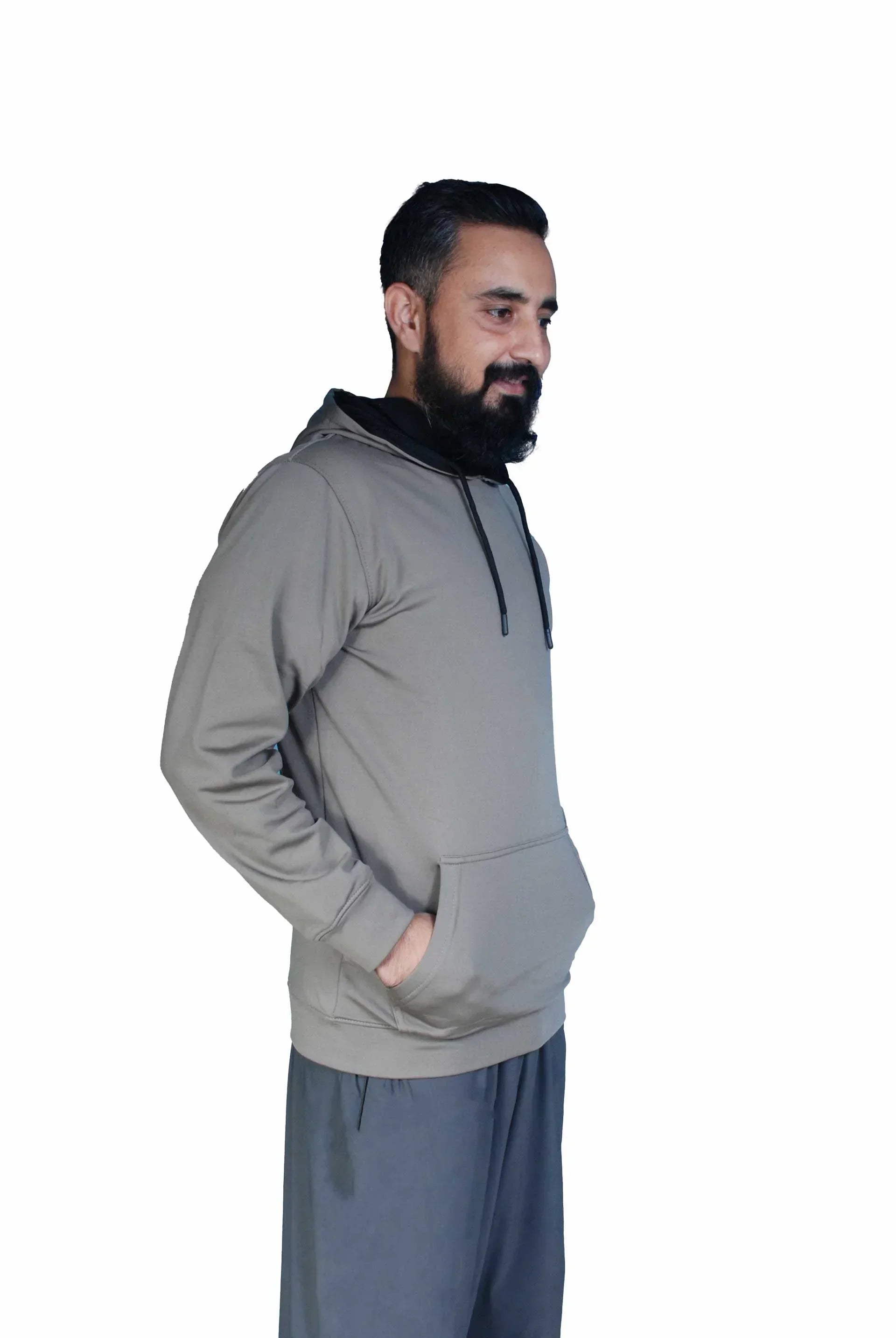 Man with beard wearing gray hoodie and dark pants standing against white background