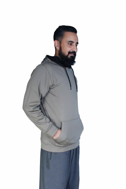 Man with beard wearing gray hoodie and dark pants standing against white background