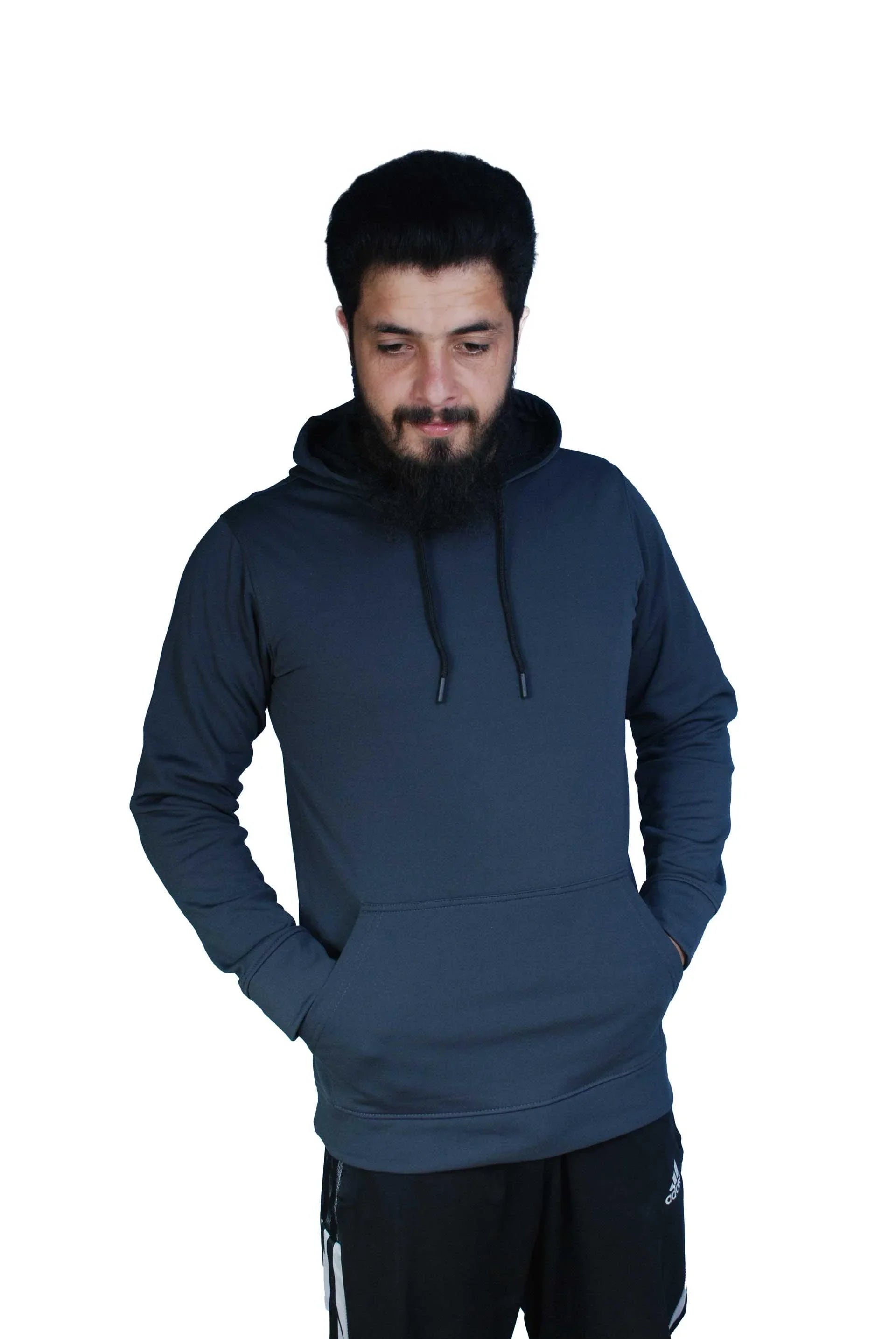 Man wearing dark gray hoodie and black Adidas track pants with hands in pockets
